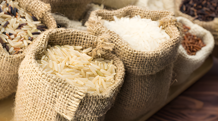 Разные виды риса в открытых мешочках из мешковины на деревянной поверхности.