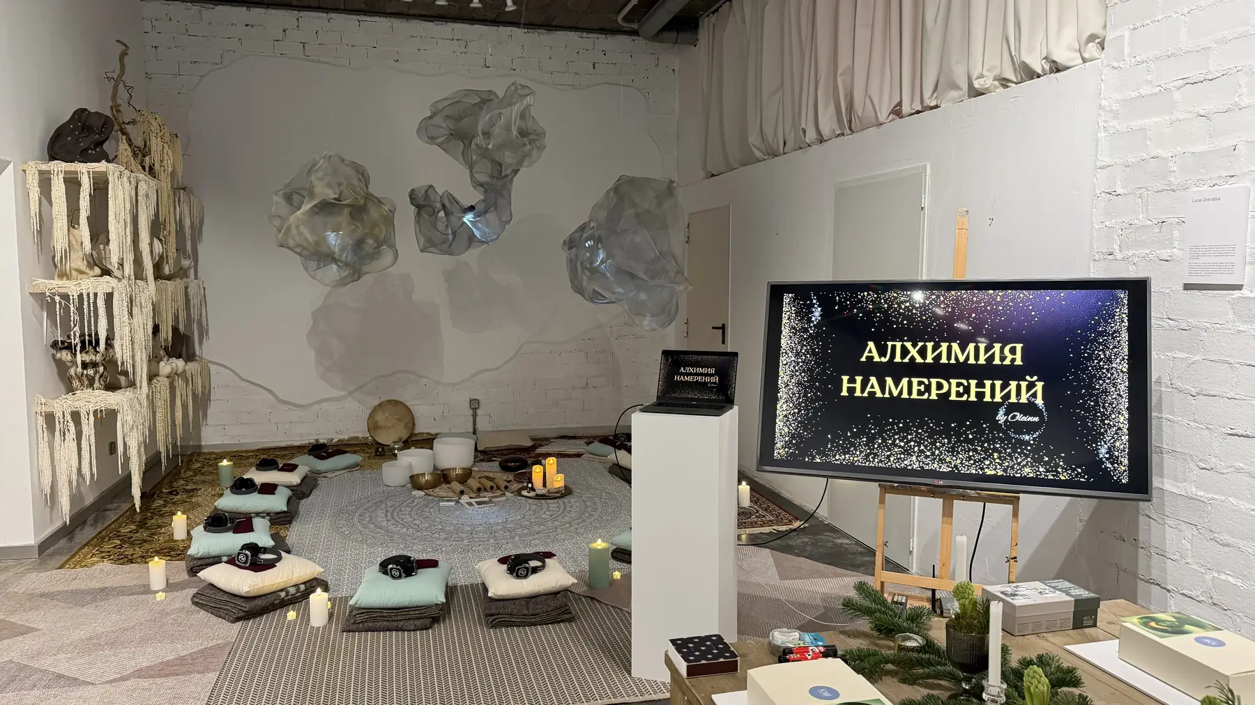 Пространство офлайн-программы «Алхимия намерений»: круг из подушек и пледов, поющие чаши, свечи и экран с названием программы