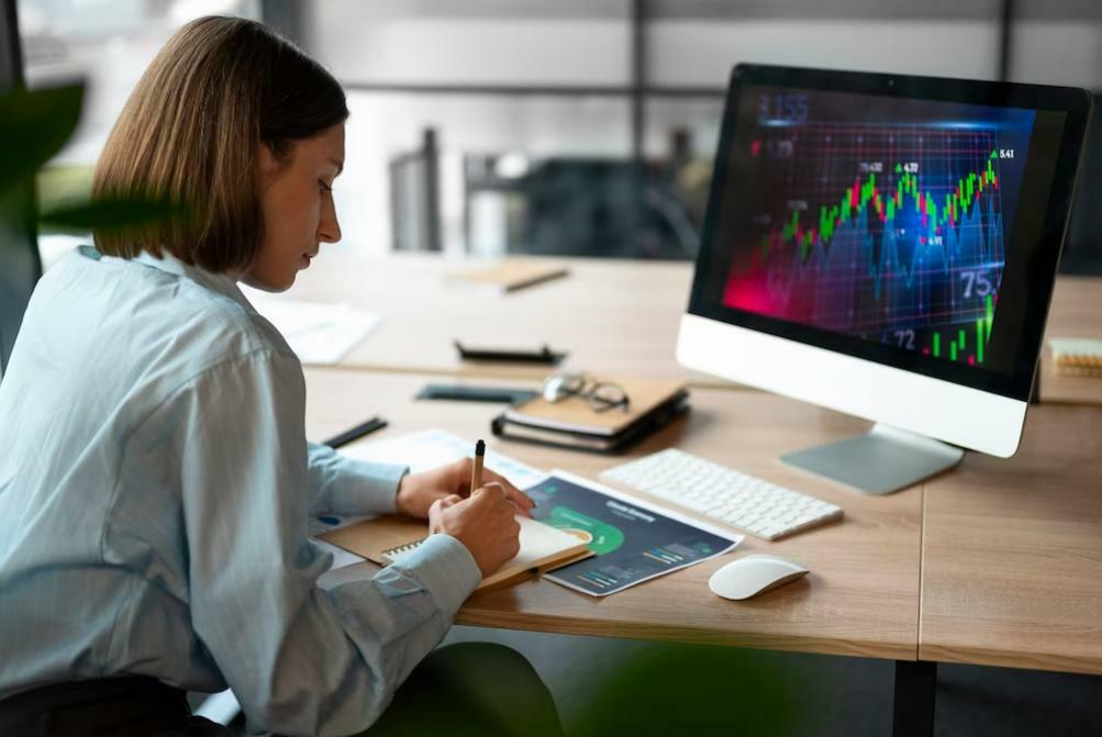 Woman taking notes in a notebook in front of a screen with price charts for technical analysis