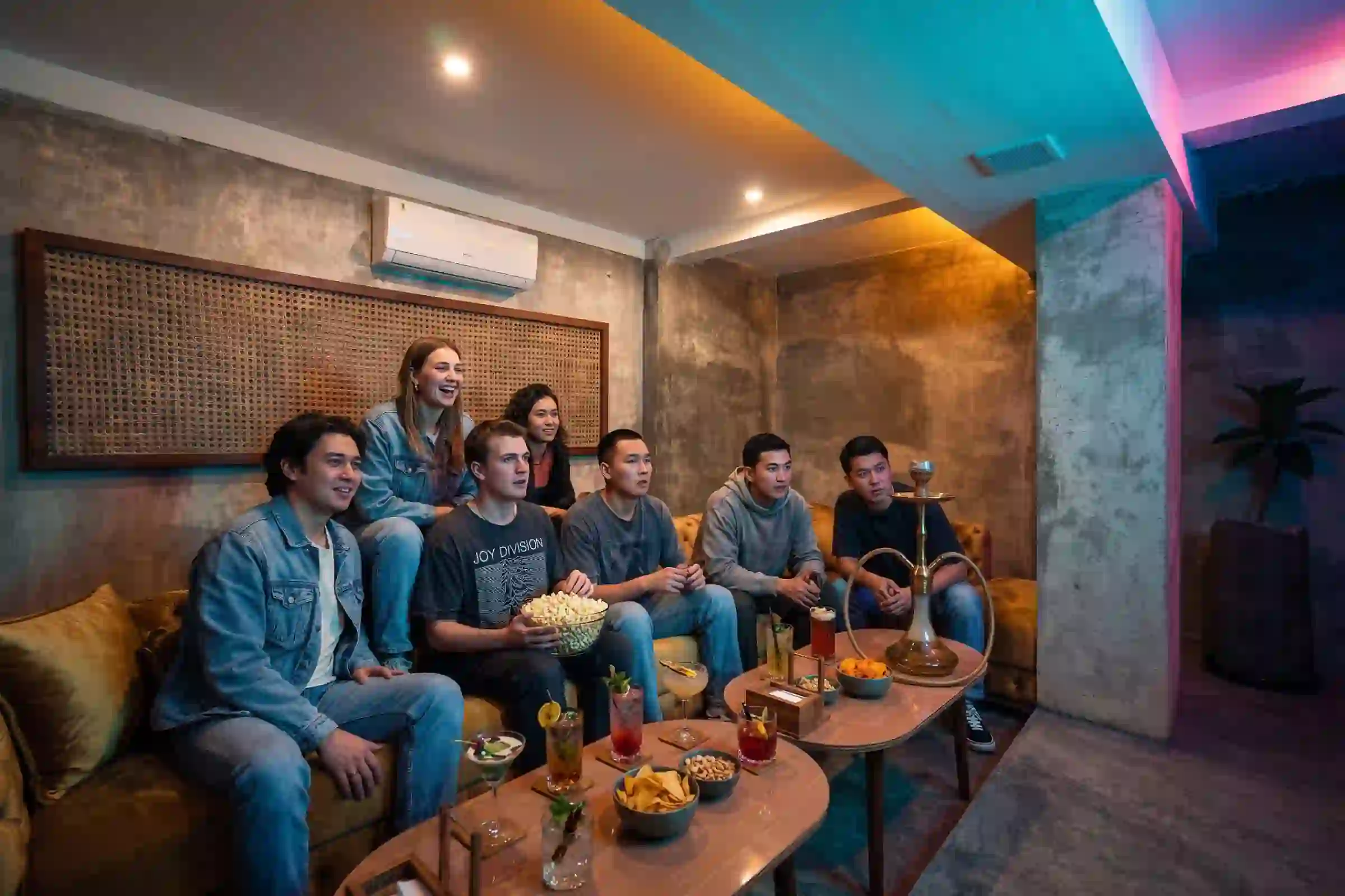A lively group of friends hanging out in the rustic VIP lounge at Eden Ubud, enjoying premium shisha and drinks while looking for where to watch a movie in Bali.