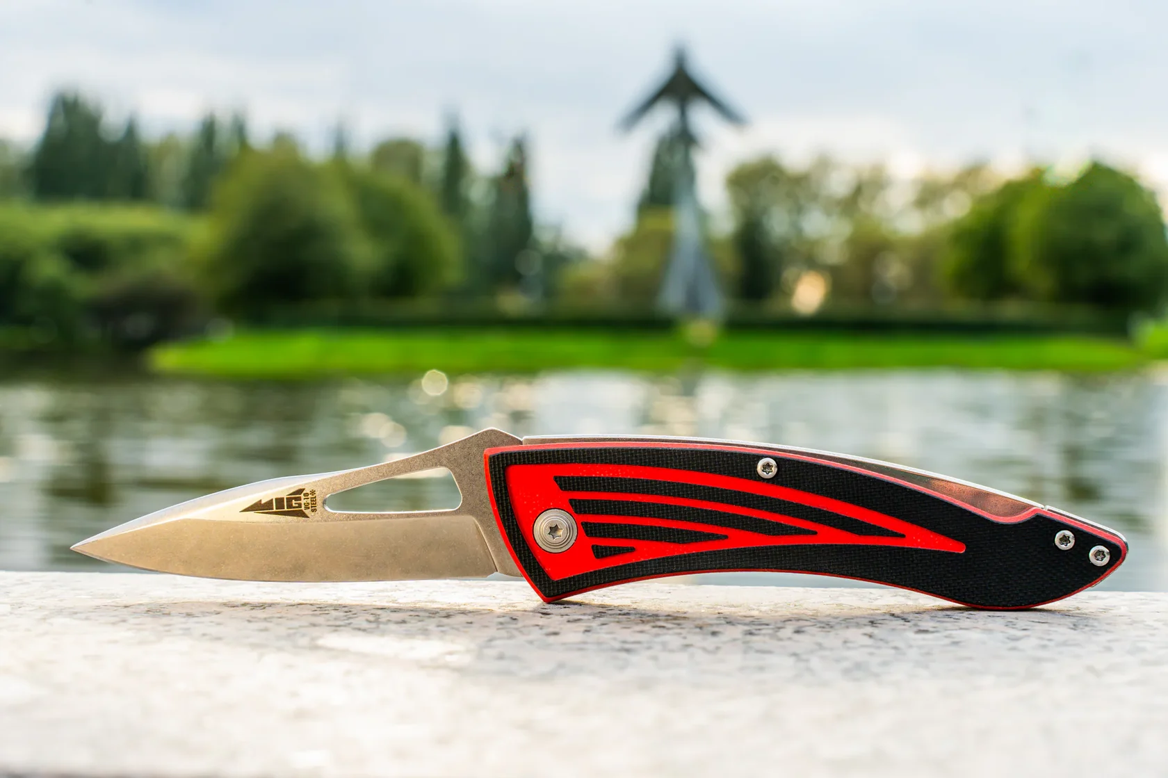 Kizlyar Supreme MiG folding knife beside a lake, showing its full aircraft-inspired profile