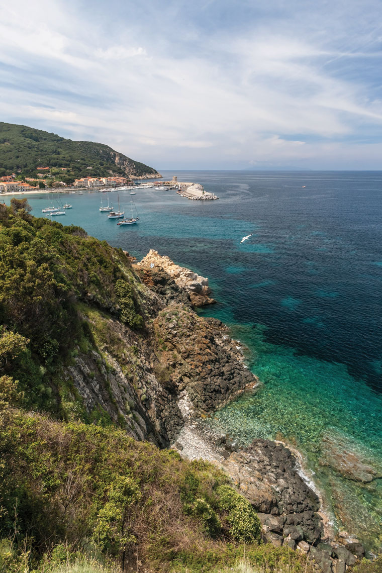 Sailboats anchor near the rocky coast of Maremma, Italy.