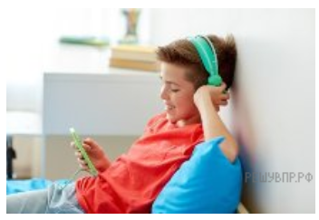 Улыбающийся мальчик лежит на кровати и слушает музыку с телефона в наушниках