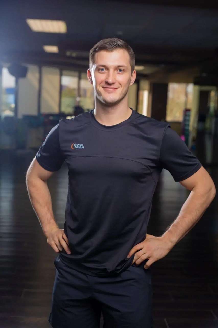 Сергей Сложеникин, персональный тренер Orange Fitness категории «элит» и автор программы НС-12, в тёмной футболке Orange Fitness в тренажёрном зале