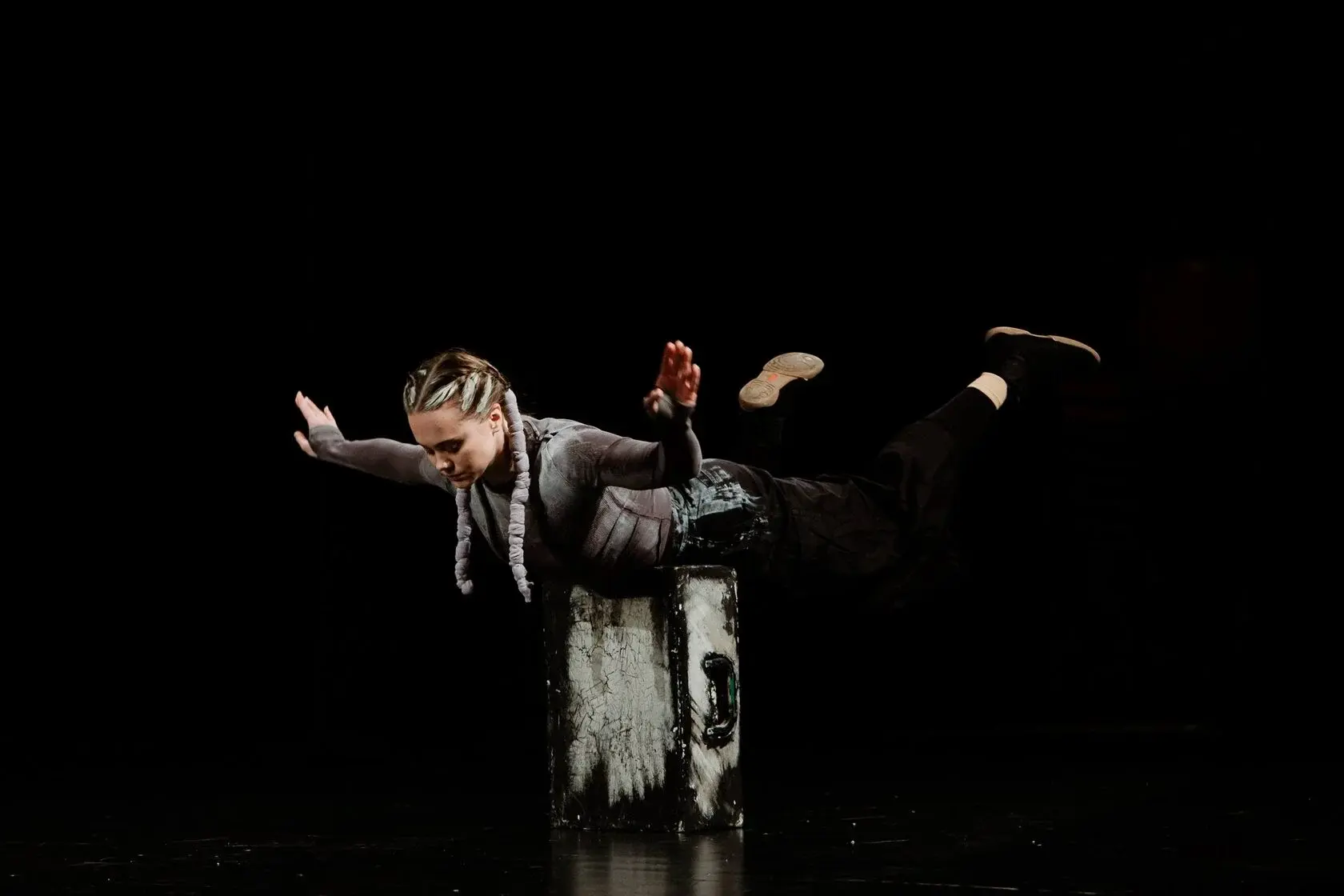 An artist balancing on a suitcase on a dark stage
