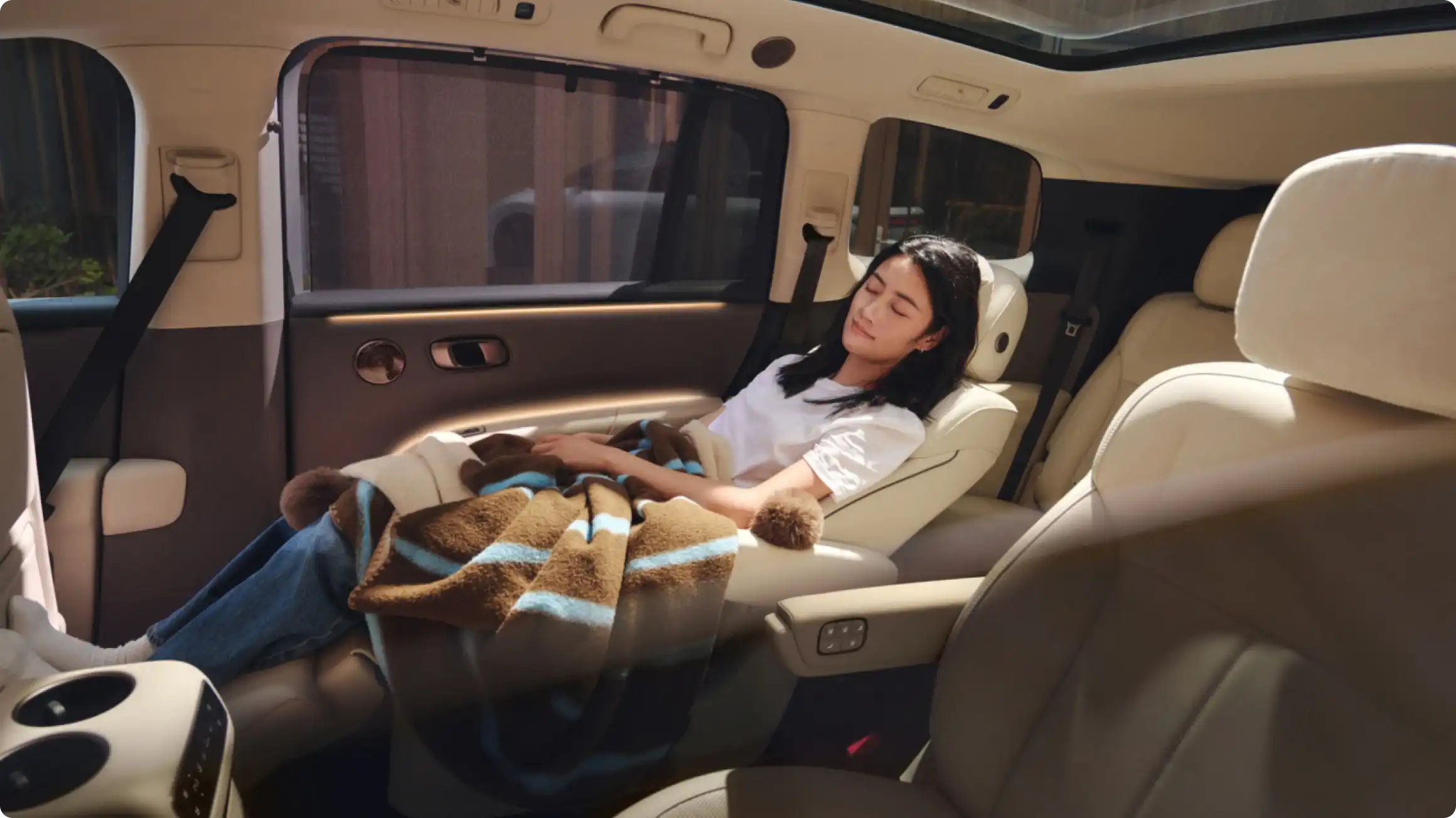 Интерьер Li Auto i9: пассажирка расслабляется в кресле второго ряда с функцией нулевой гравитации, укрытая пледом, на фоне премиальной отделки салона.