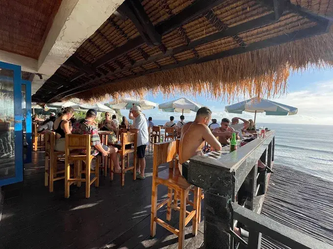 Guests taking in the iconic cliffside ocean views from the wooden deck at Single Fin, famously known as one of the best bars in Bali for sunset and surf watching.