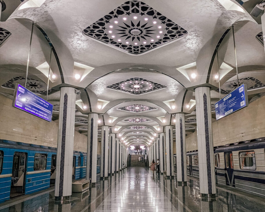 Tashkent metro station interior with advertising posters along the walls and a blue metro train at platform