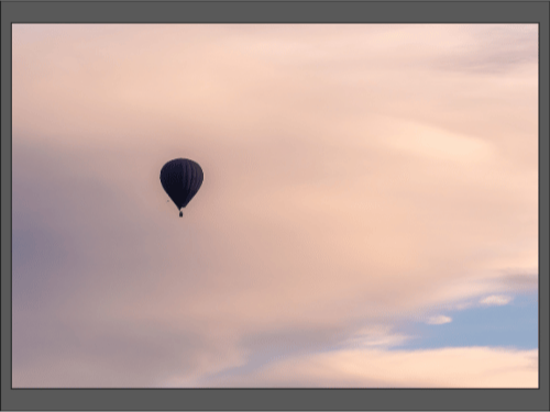 Воздушный шар поднимается в небо среди мягких облаков.