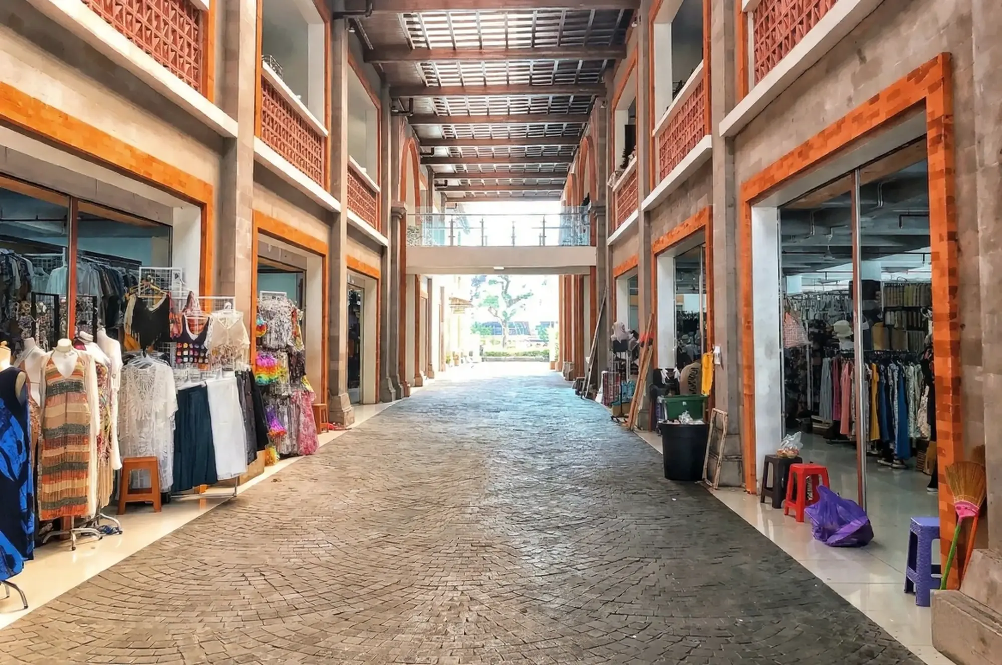 A view down the quiet, spacious brick corridors of the indoor Ubud Art Market building, lined with neat vendor stalls selling clothing and local goods.