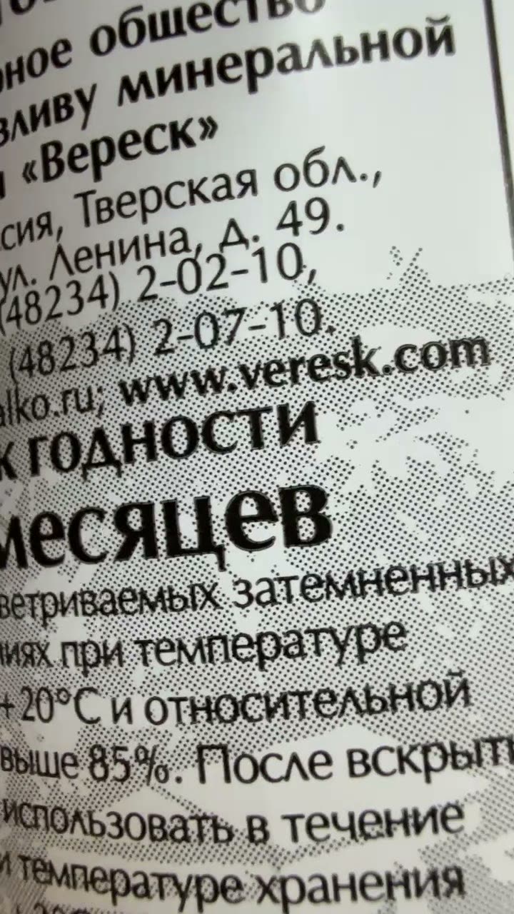 Оборот этикетки бутылки воды вблизи: мелкий чёрный текст с чёткими краями поверх серого растрового пейзажа