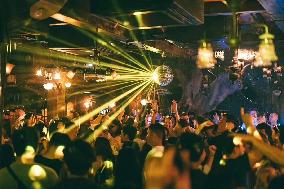A lively crowd dancing under a glowing disco ball at a vibrant nightclub, keeping the energy high after their pre drinks.