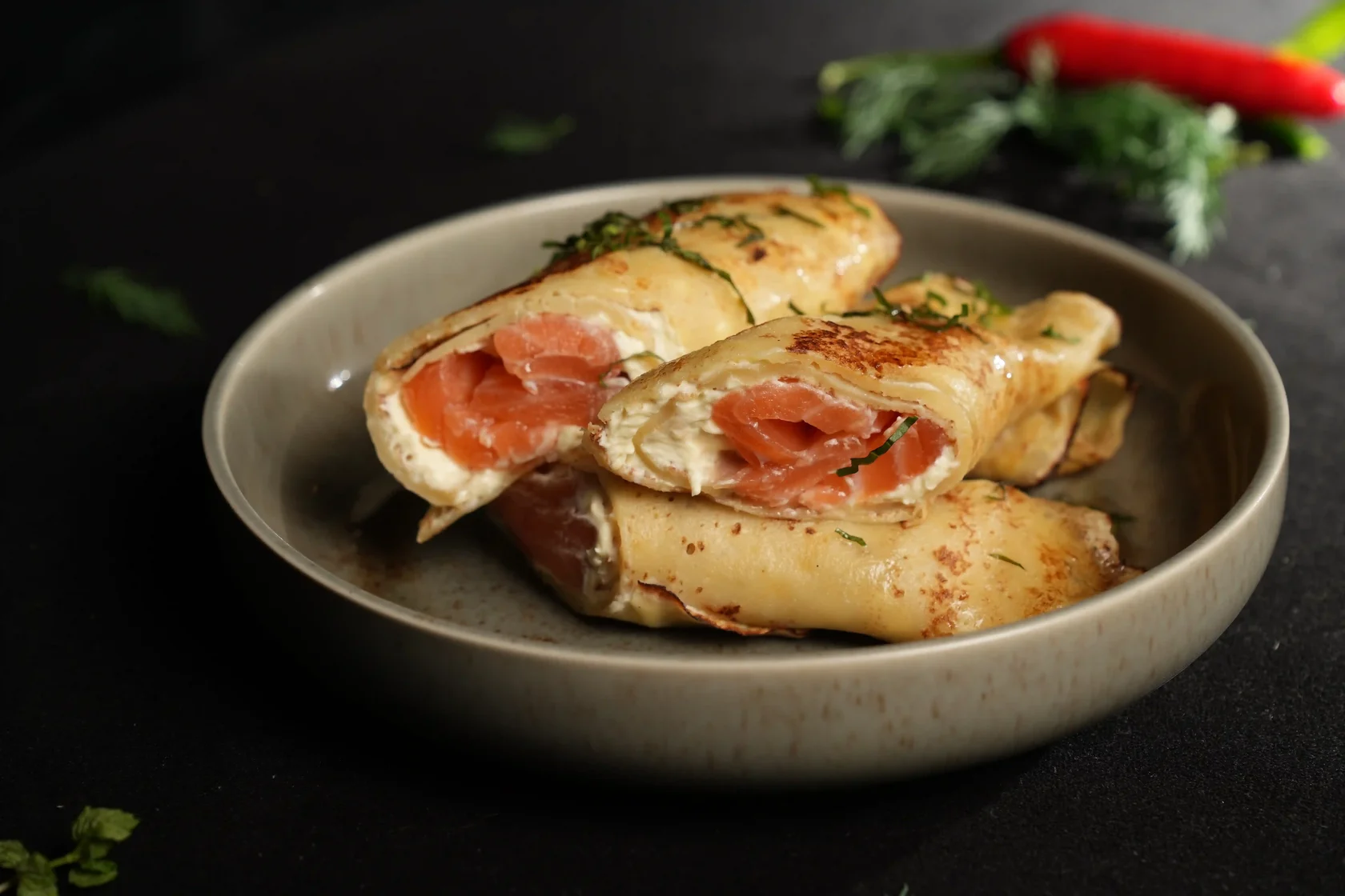 Salted salmon crepes filled with cream cheese and garnished with fresh herbs