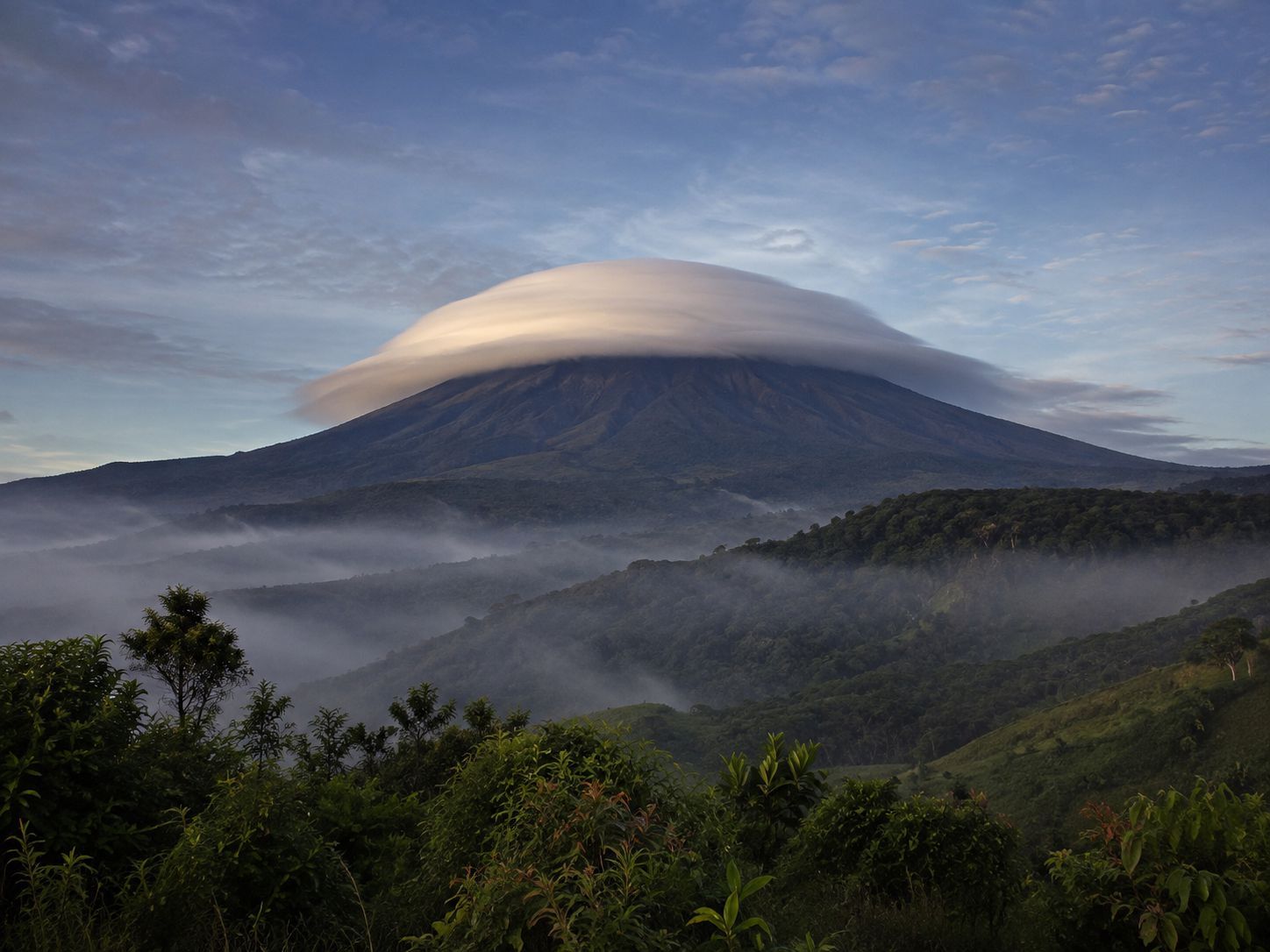 Awan topi putih membungkus puncak gunung Indonesia pada pagi hari yang tenang