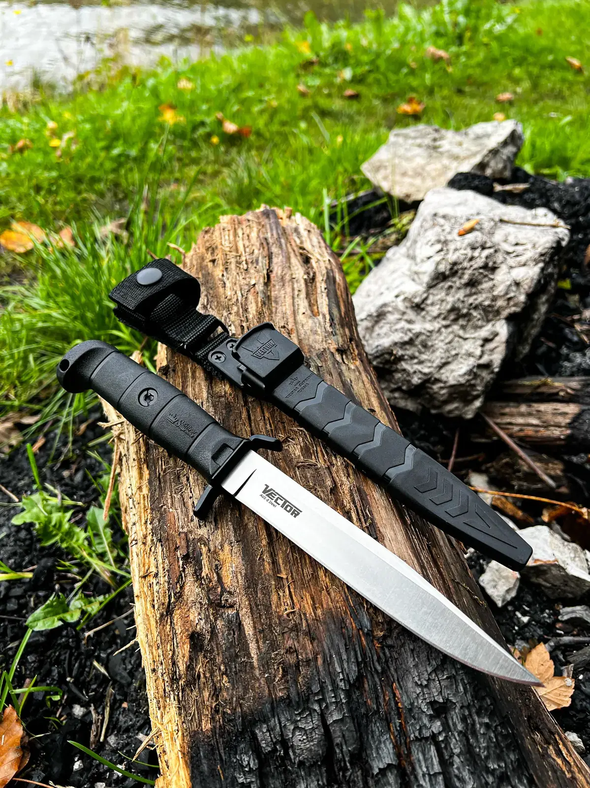 Black Kizlyar Supreme Vector and sheath on a charred log outdoors