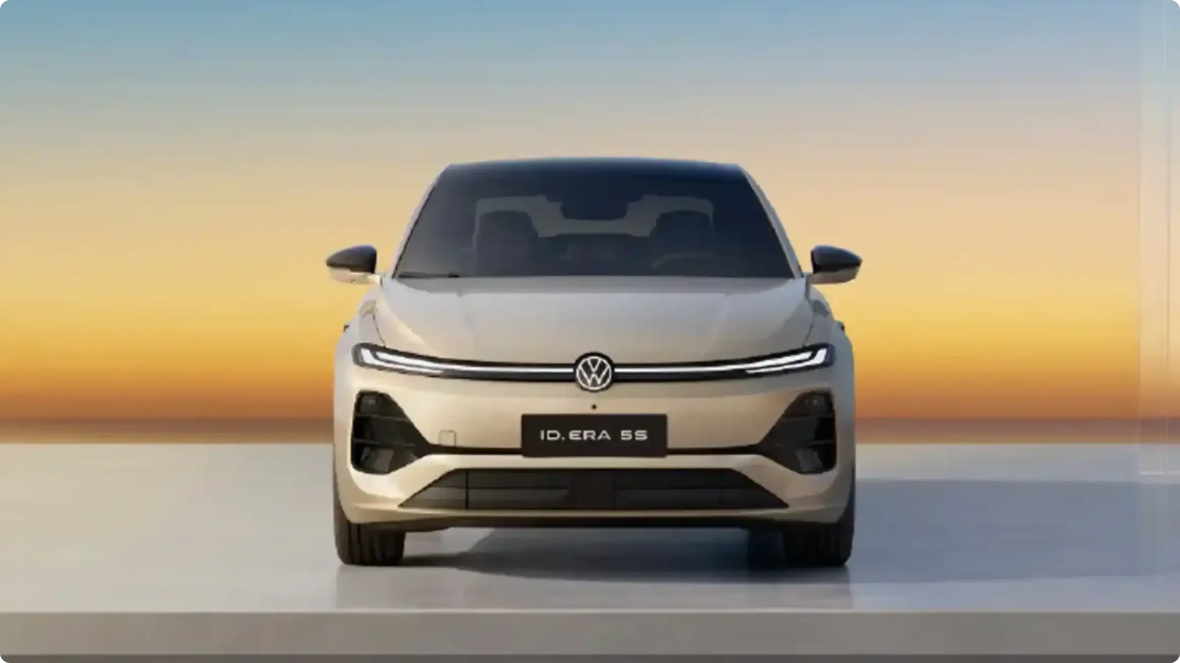 Volkswagen ID. ERA 55 в бежевом цвете, фронтальный вид: светодиодная полоса с логотипом VW, черные зеркала и современный бампер на фоне заката.