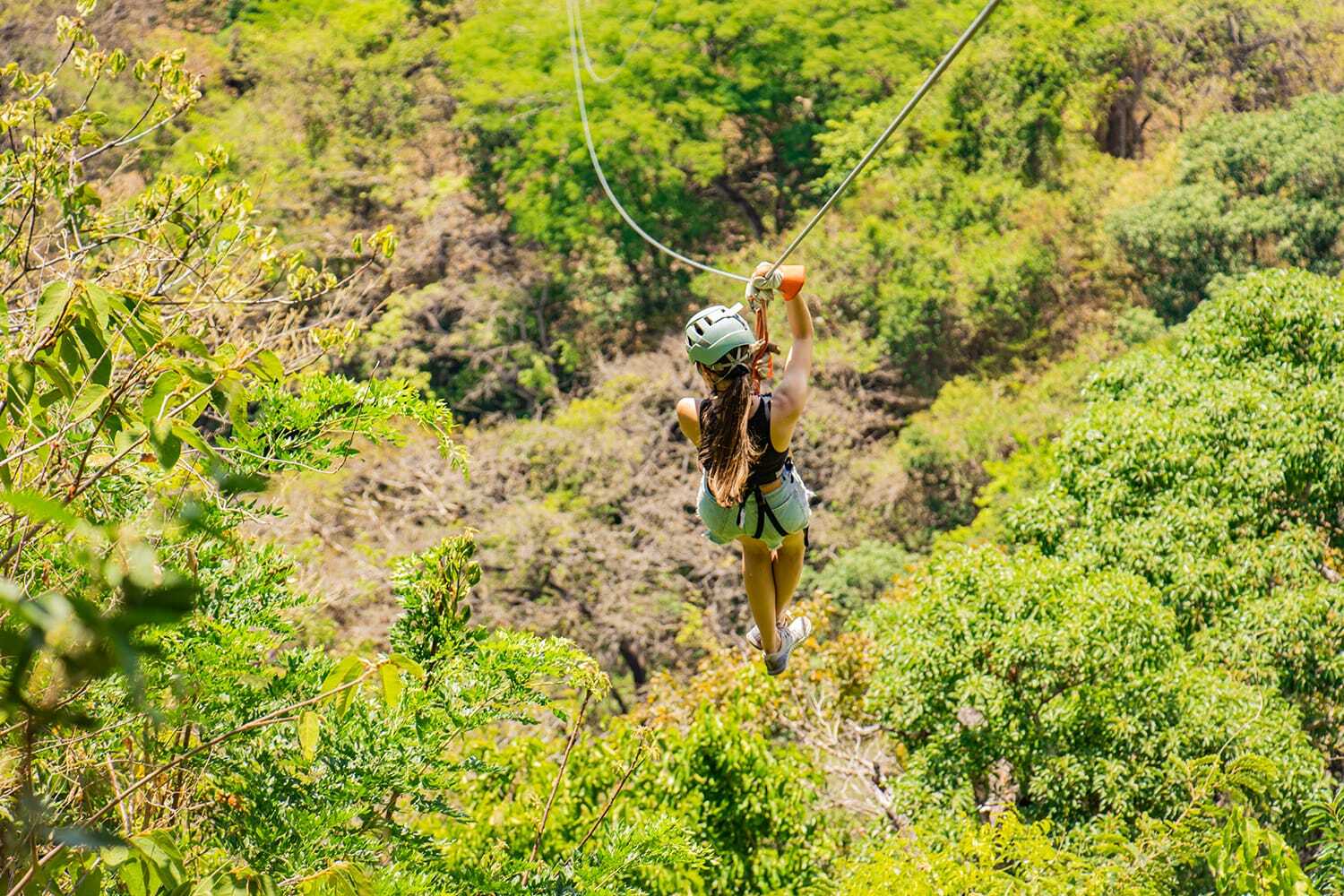 Helmeted participant traveling along a zipline above green vegetation