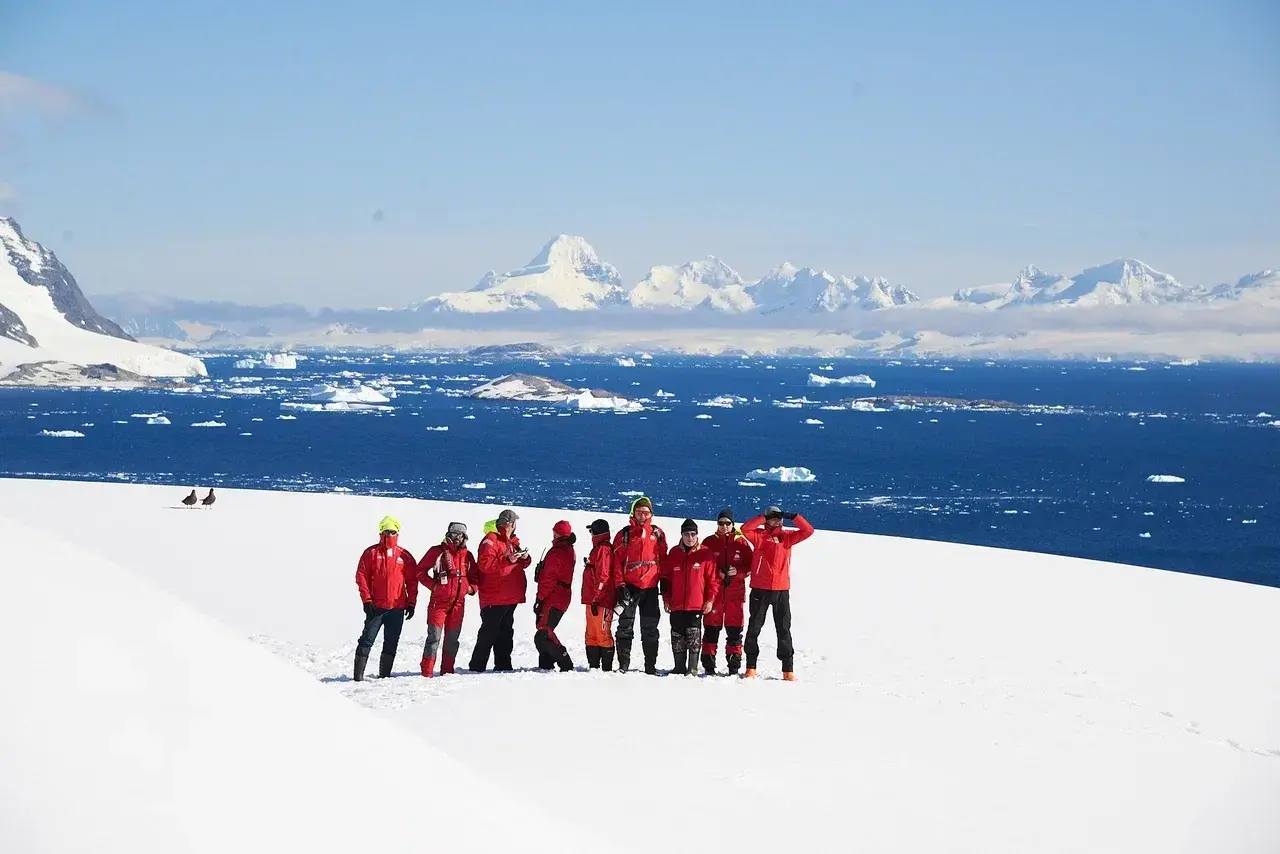 Antarctica expedition participants exploring a snowy landscape overlooking iceberg-filled waters and dramatic mountains of the Antarctic Peninsula.