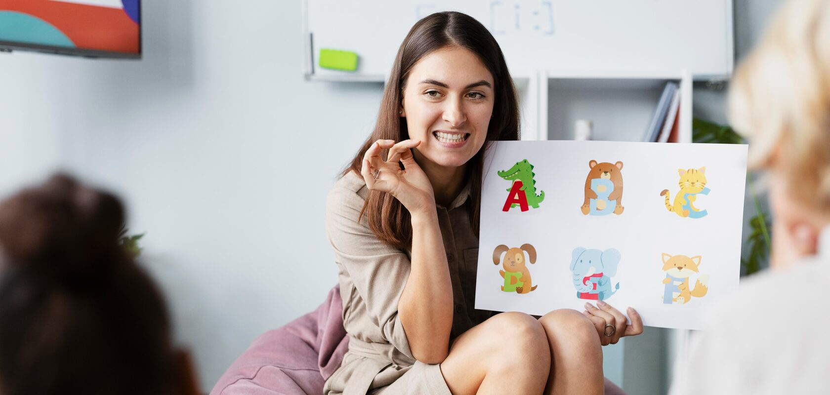 Женщина-логопед с доброжелательной улыбкой показывает детям, как правильно выговаривать букву, держа в руках яркий алфавит. Ее жесты и выражение лица передают терпение и профессионализм, создавая атмосферу доверия и увлеченности. Дети внимательно слушают и повторяют, что подчеркивает важность таких занятий для развития речи. Этот момент идеально подходит для статей о логопедических методиках, развитии речи у детей, образовательных программах или работе с дошкольниками. Картинка вызывает положительные эмоции и напоминает о том, как важно помогать детям осваивать новые навыки в комфортной и поддерживающей обстановке.