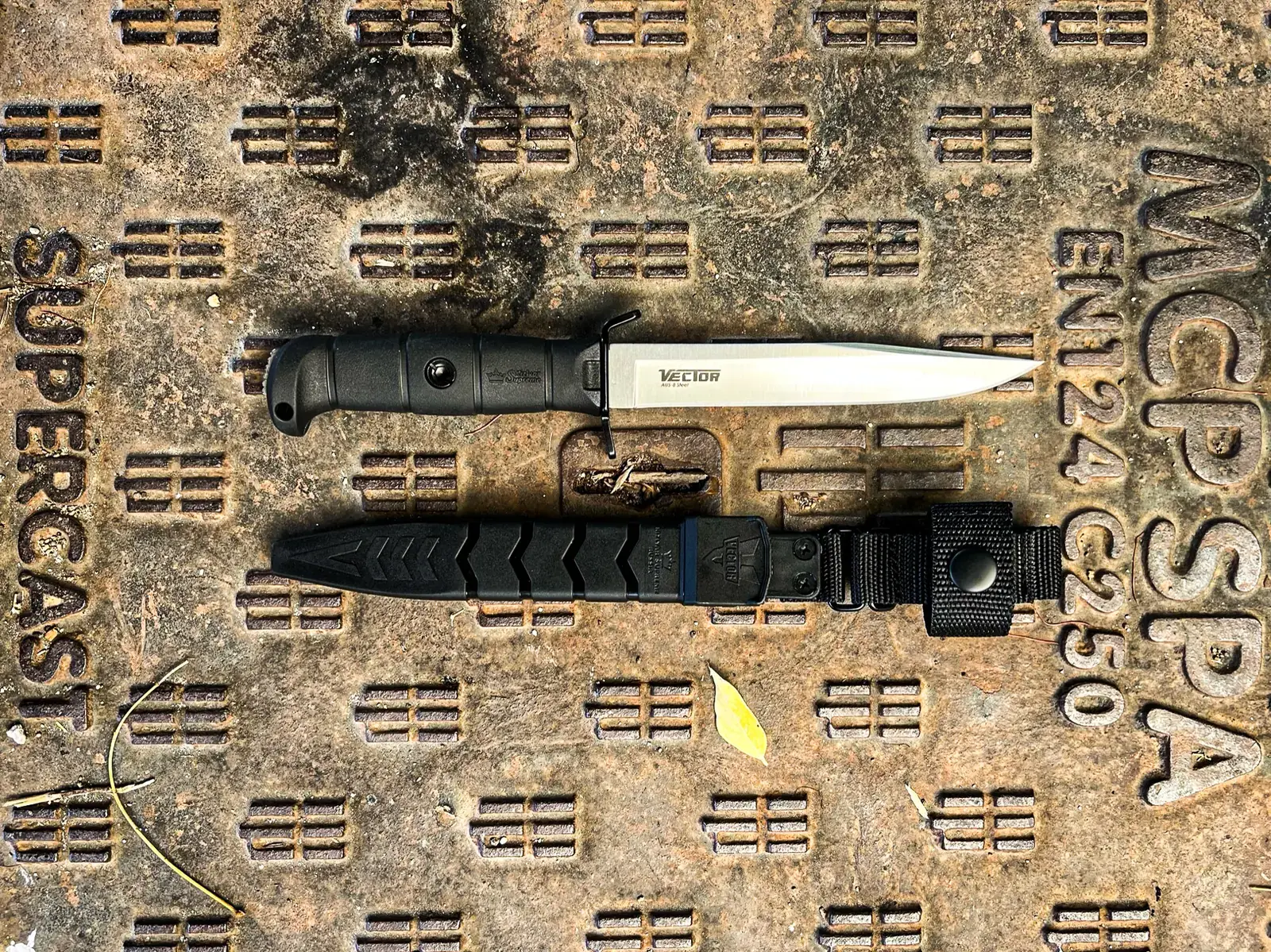 Black Kizlyar Supreme Vector and sheath shown full length on an industrial surface