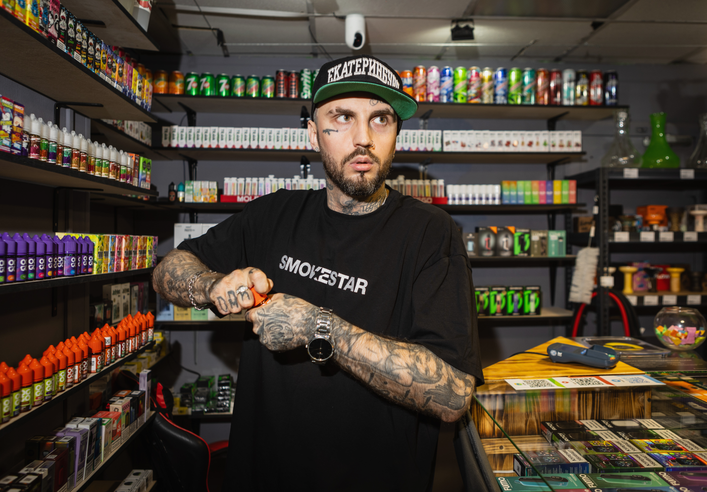 Мужчина в кепке SMOKESTAR открывает жидкость для вейпа