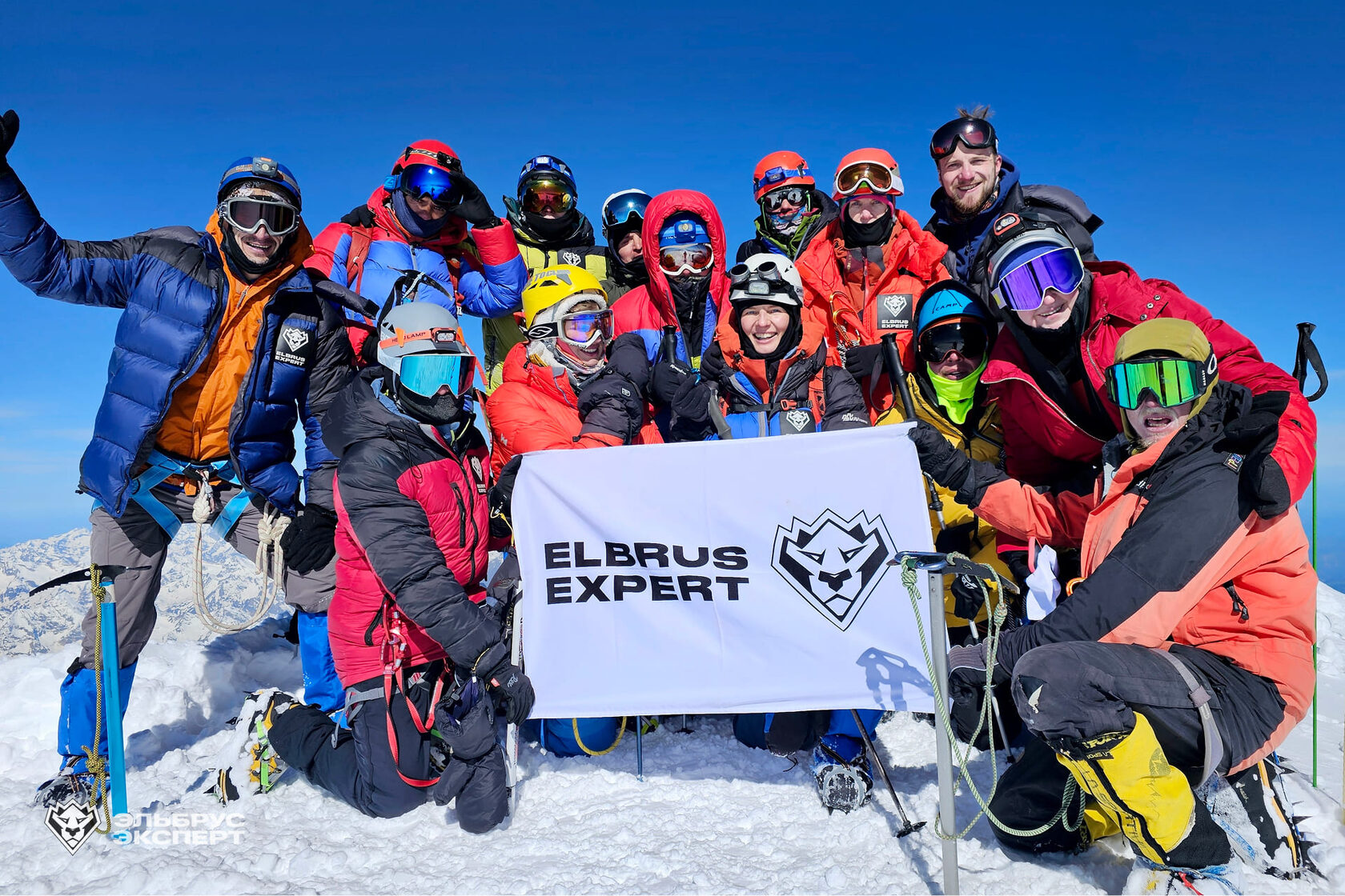 Group with an Elbrus Expert flag on a snowy summit under a blue sky