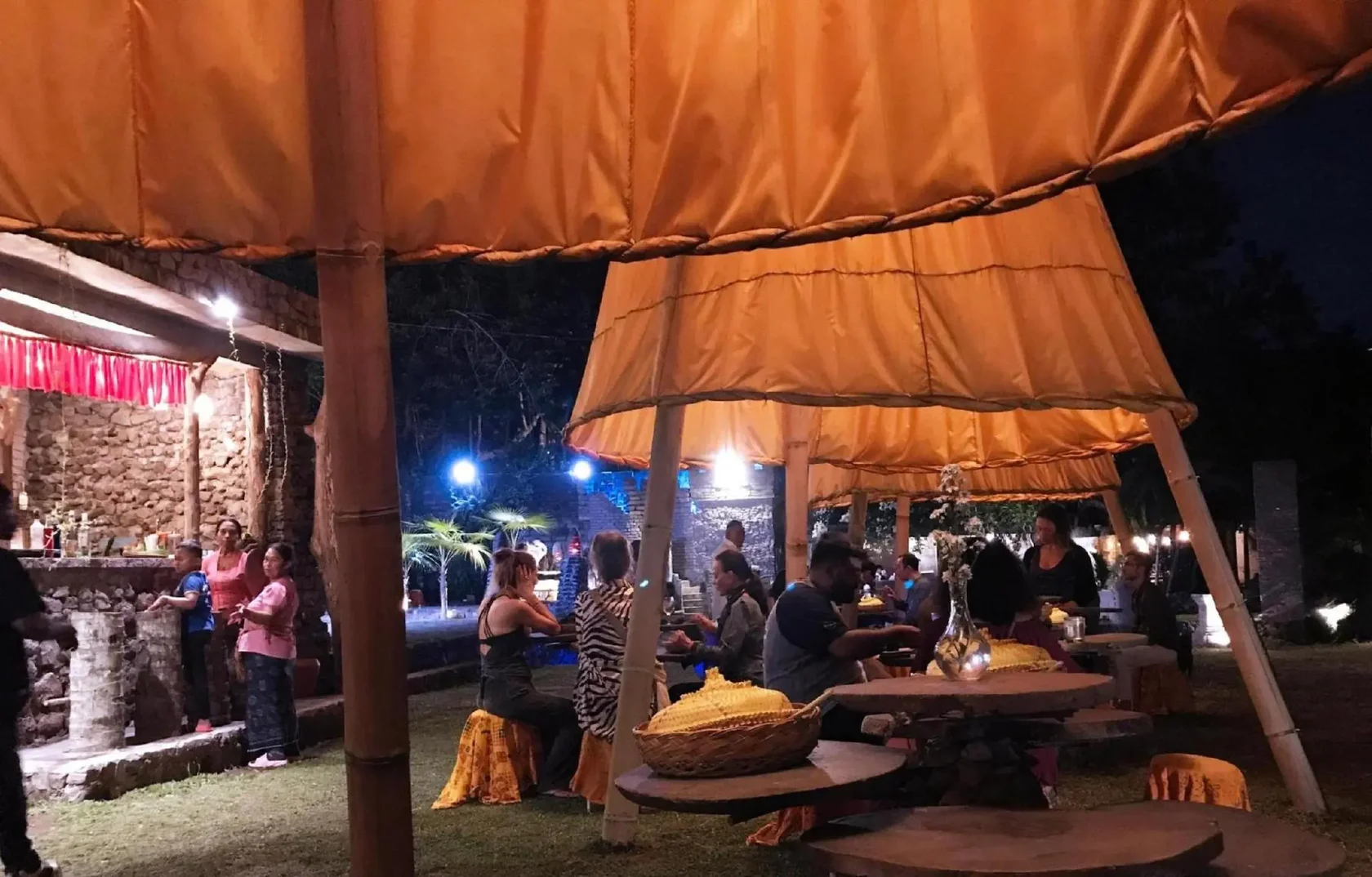 A lovely outdoor setting for a top dinner in Ubud, featuring guests dining under warmly lit traditional yellow umbrellas with a relaxed and welcoming evening atmosphere.