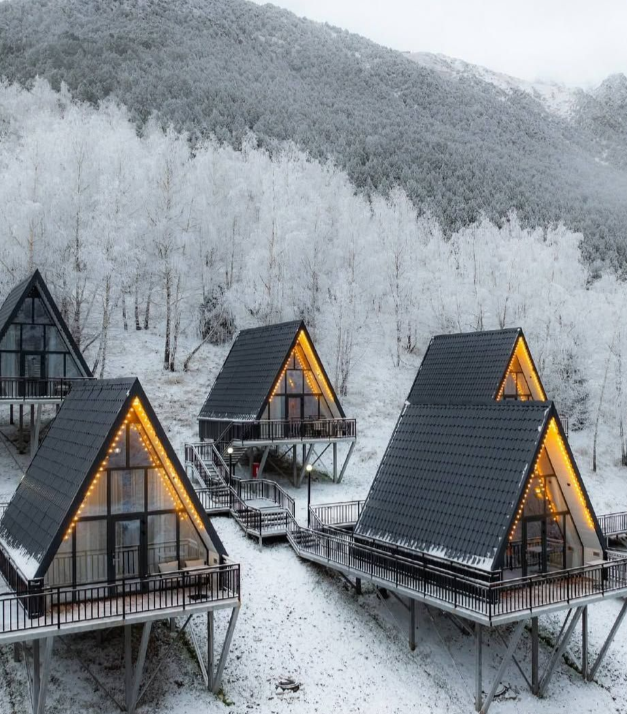 Несколько A-frame домов в снежных горах с подсветкой