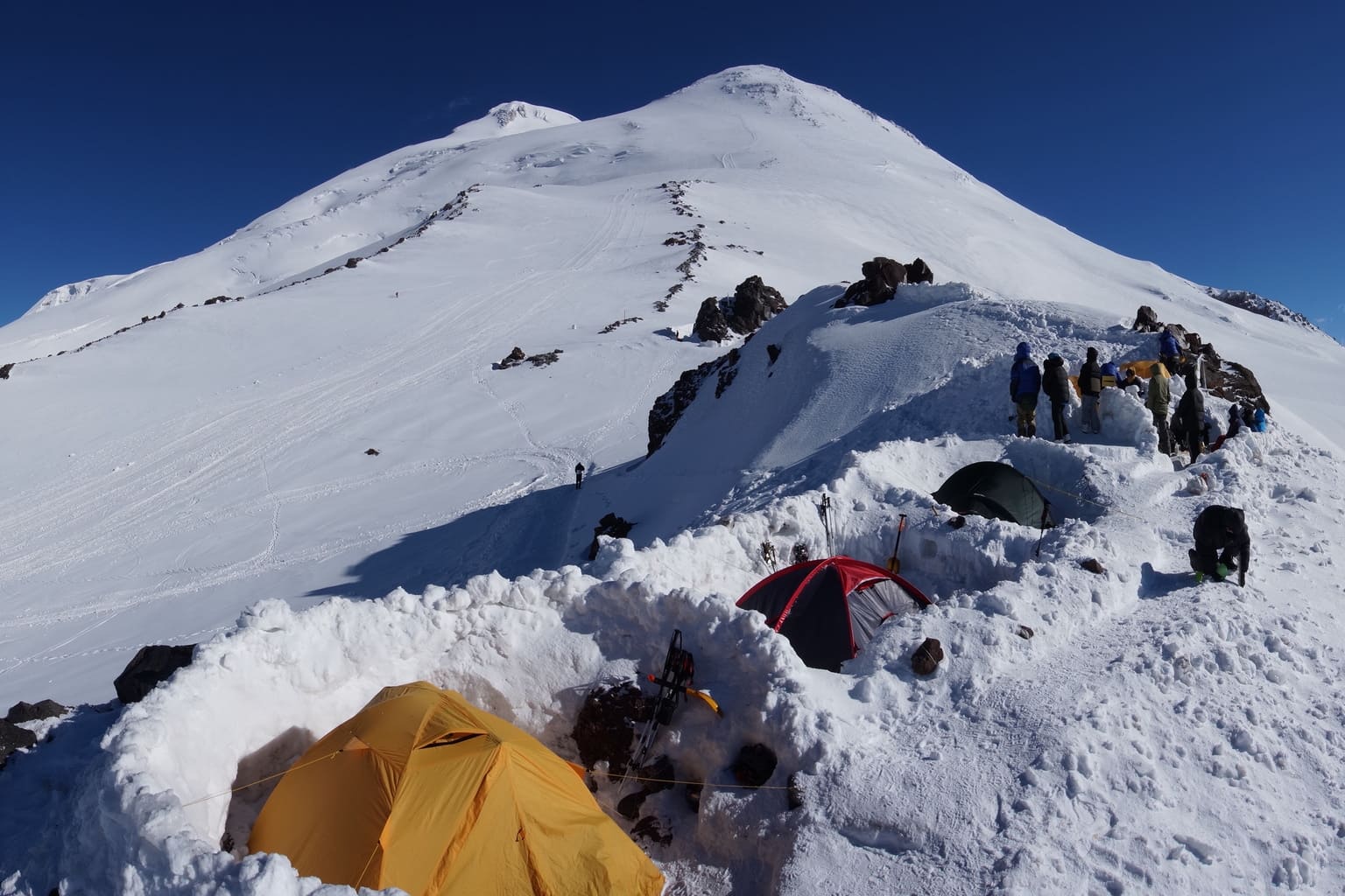 Tents pitched in the snow on the Elbrus slope with the summit above