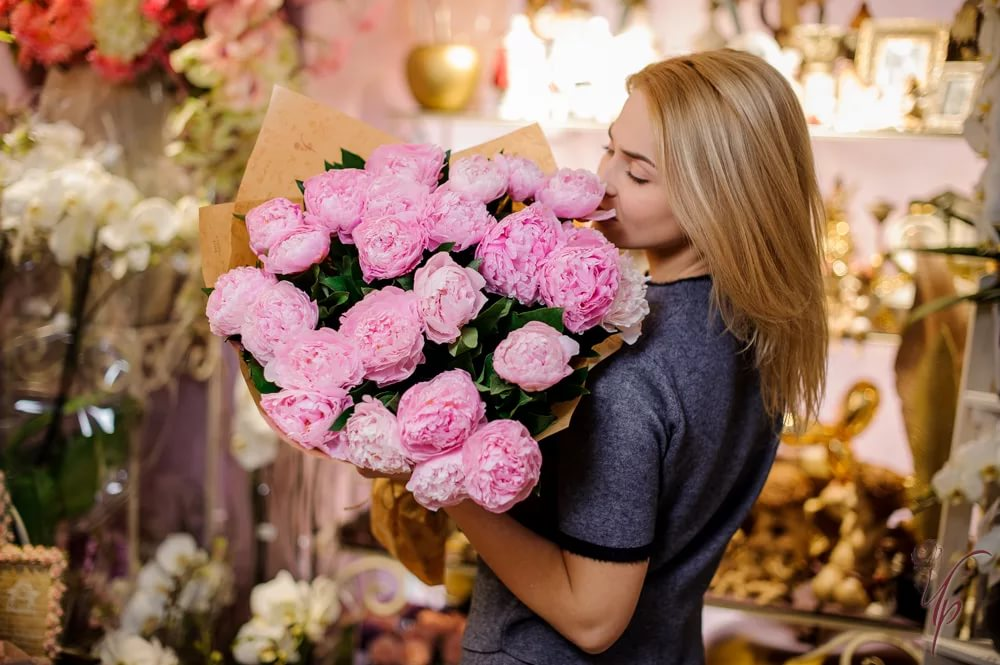 Большой букет из розовых пионовидных роз в упаковку в руках флориста