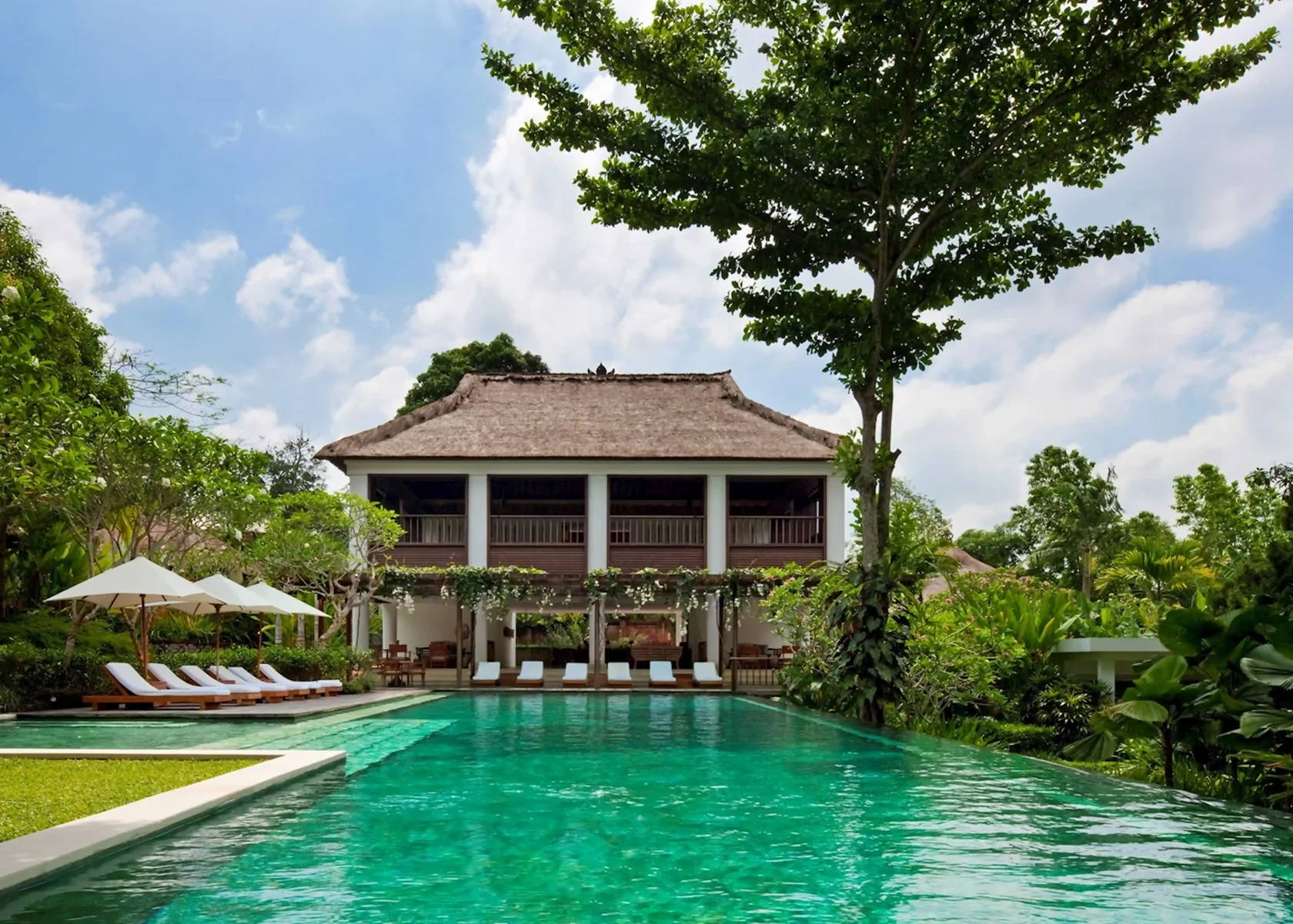 Serene emerald swimming pool reflecting a beautiful traditional two-story Balinese villa surrounded by lush gardens at Como Uma Ubud.