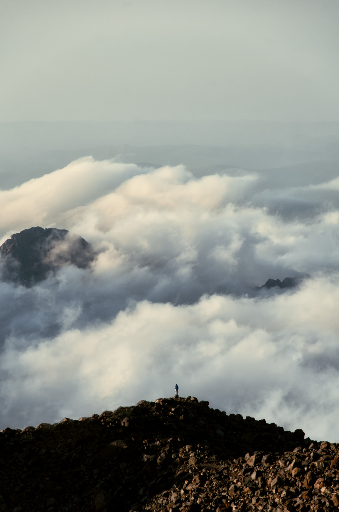 Гора Эльбрус. Альпинист стоит на скалах над облаками. Северные склоны Эльбруса. Фотограф Севальнев Ян.