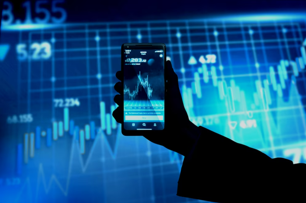 Una mano sosteniendo un teléfono móvil con gráficos de trading en Binance, en alto contraste con el fondo que posee una imagen similar.