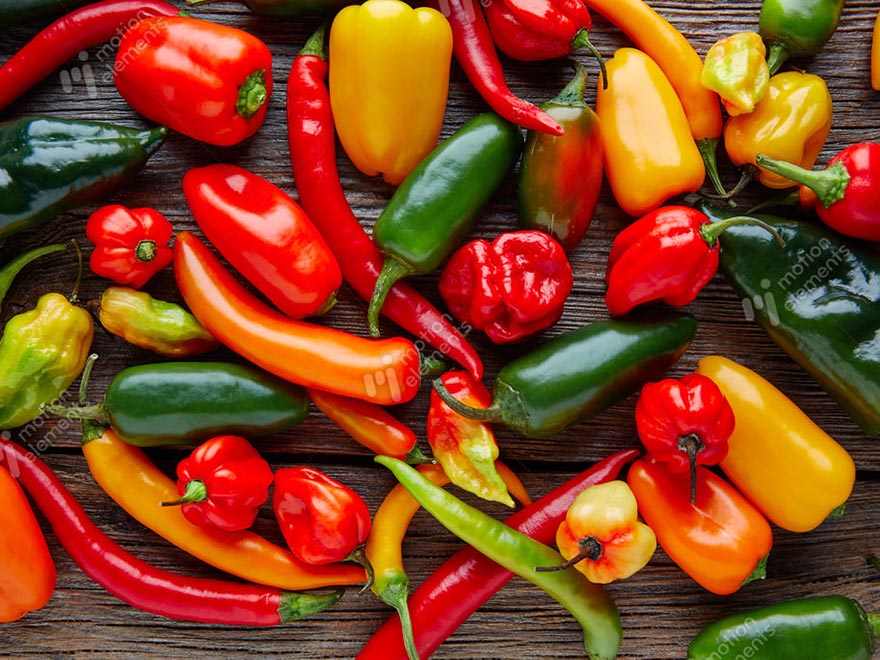 A vibrant assortment of bell peppers and chili peppers in various colors, including green, red, yellow, and orange, arranged on a wooden surface, showcasing the diversity of pepper varieties ideal for home gardening.