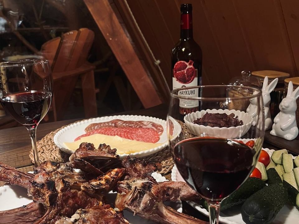 мясо, закуски и бокалы вина при вечернем свете в шале
