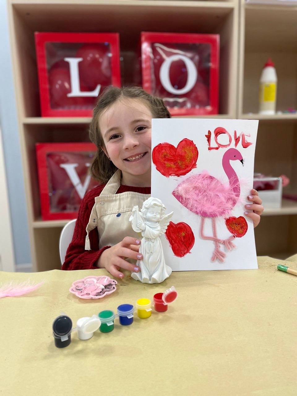 Девочка держит поделку с фламинго и сердечками ко Дню святого Валентина в детском саду Magic Beans