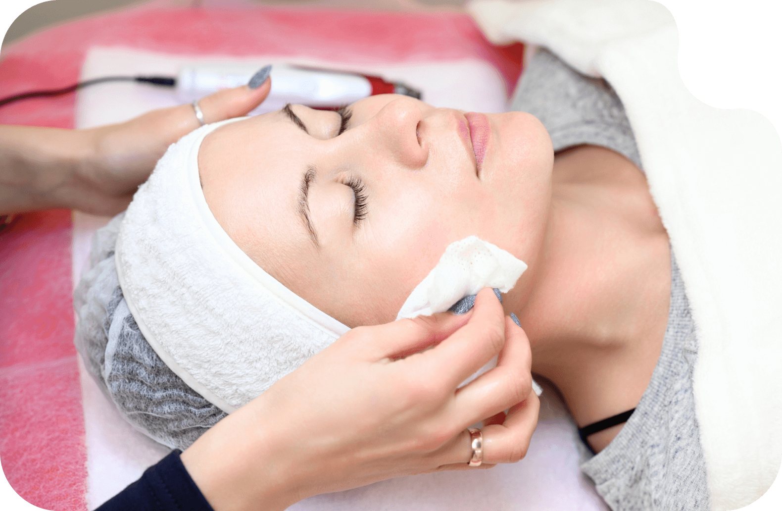 Девушка лежит на косметических процедурах, рука косметолога протирает её лицо серебряной водой