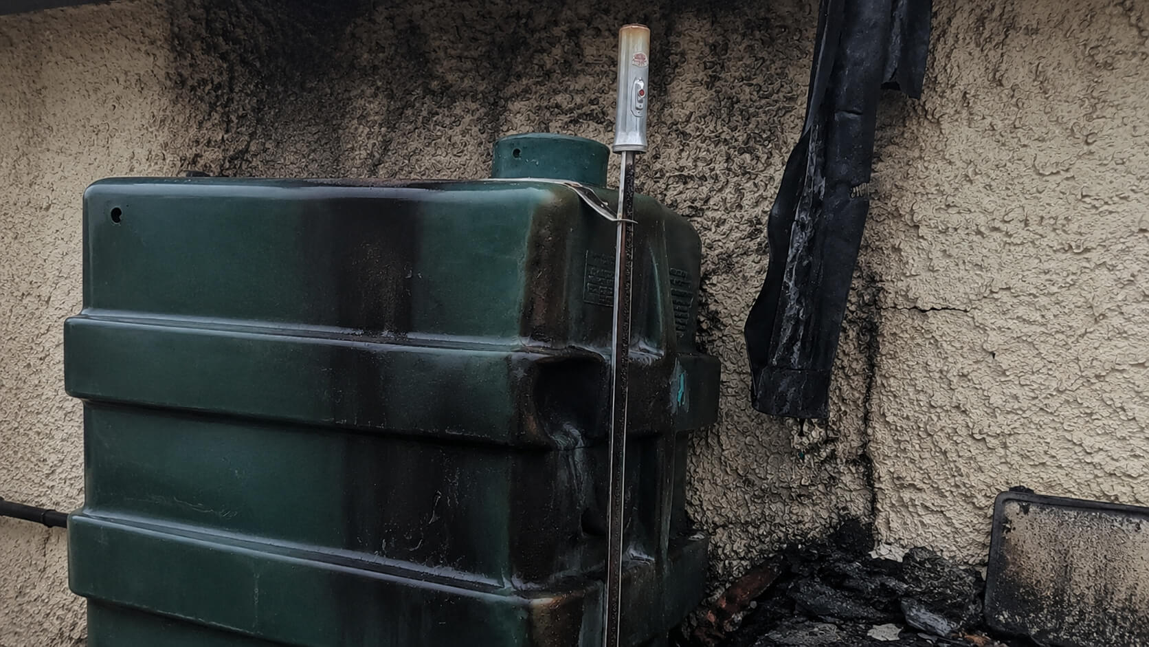 Oil tank showing heat damage and deformation after a shed fire