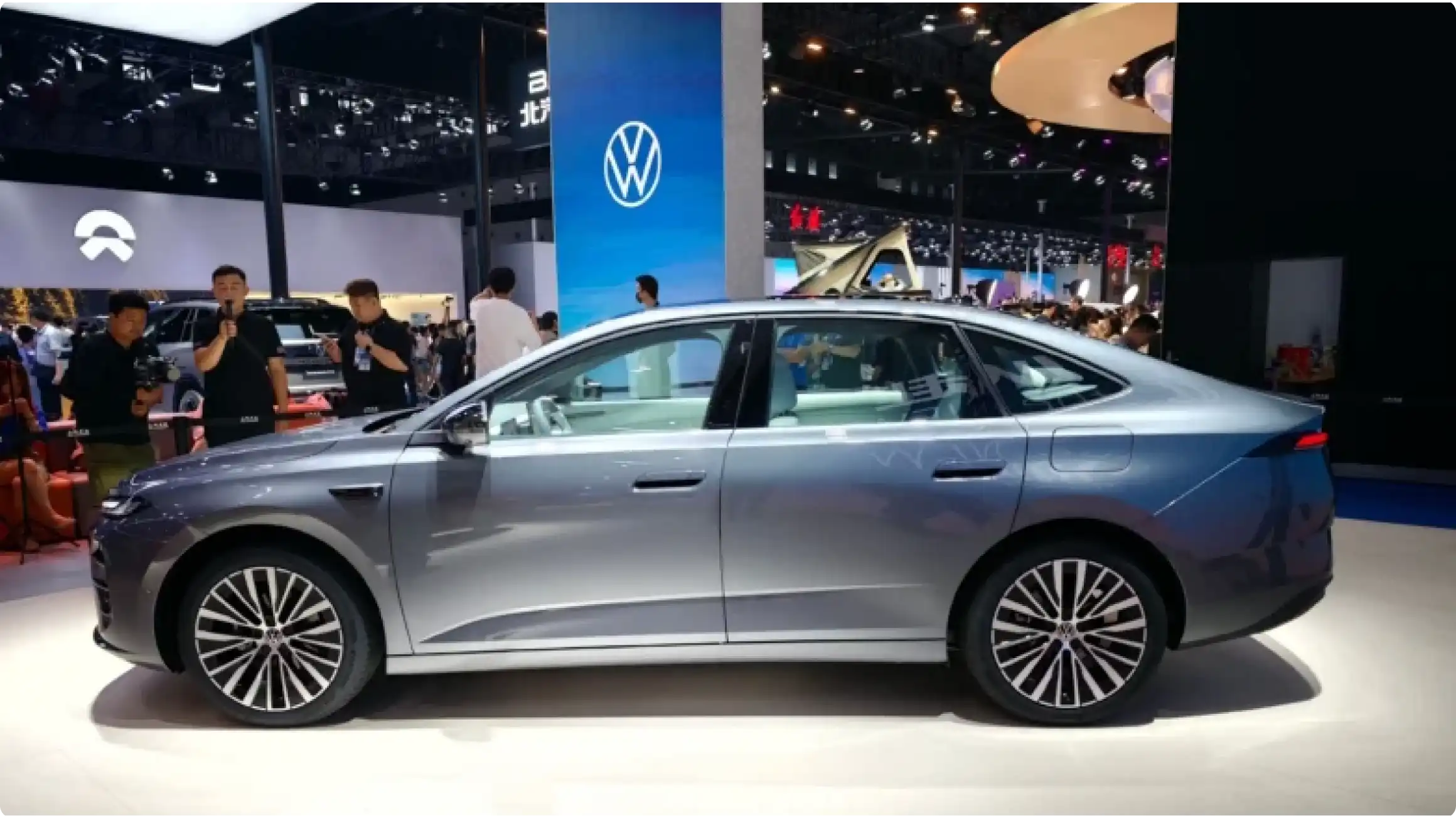 Боковой профиль седана Volkswagen ID. Era 5S в серо-синем цвете на автосалоне: полускрытые дверные ручки, элегантная линия крыши и аэродинамичные легкосплавные диски.