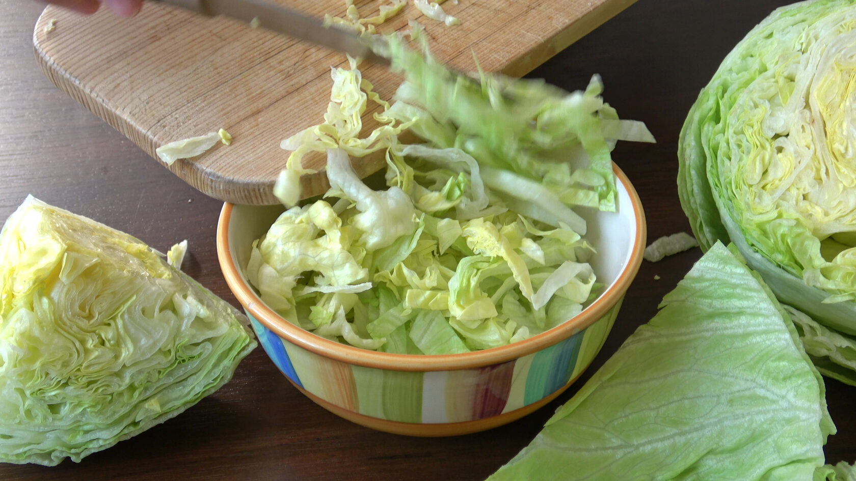 Chopped iceberg lettuce in a colorful bowl with a knife and cutting board, illustrating preparation for fresh salad and home gardening practices.