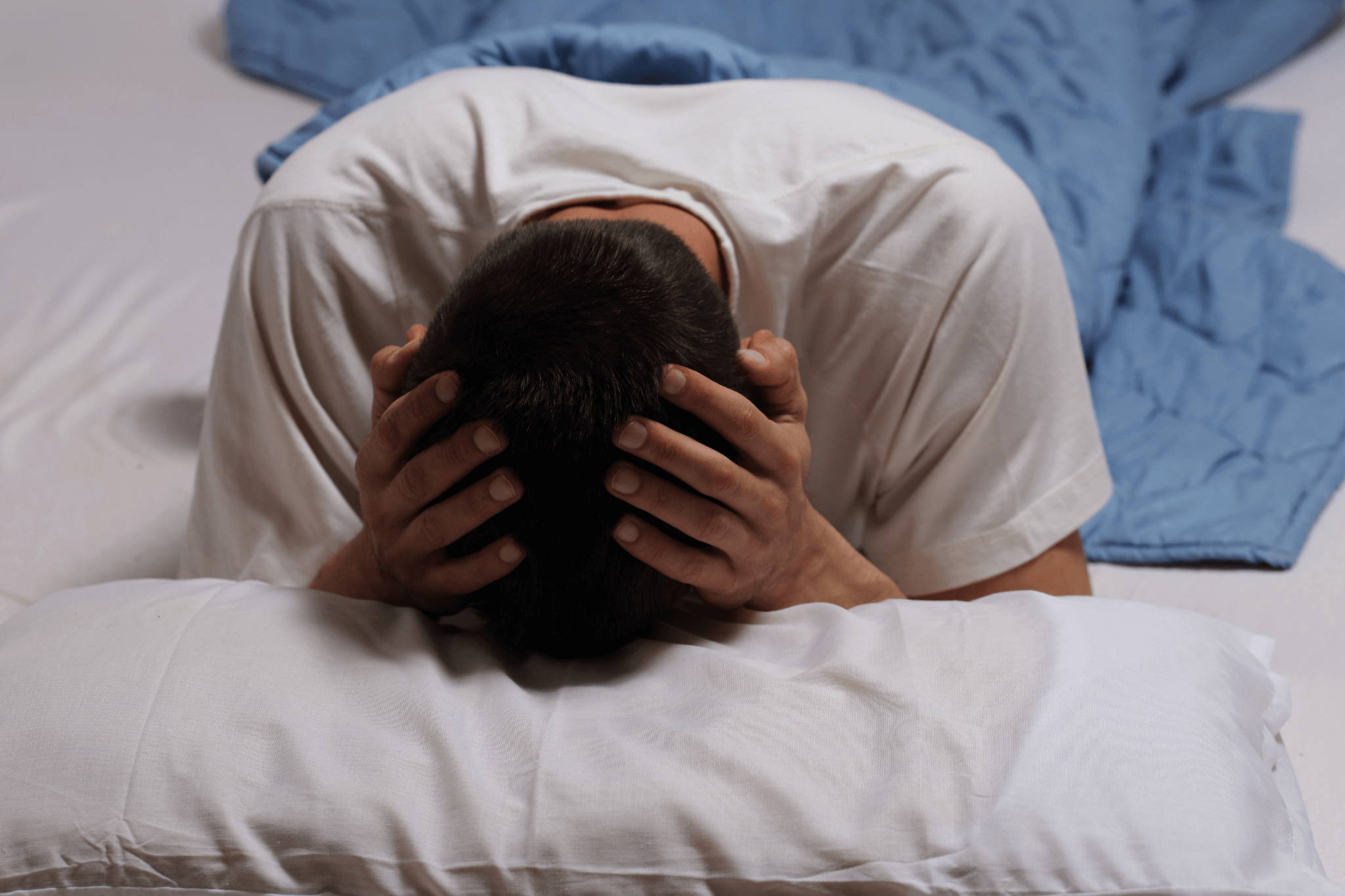 Mann in Bett legt Hände um seinen Kopf und deutet Schlafprobleme an