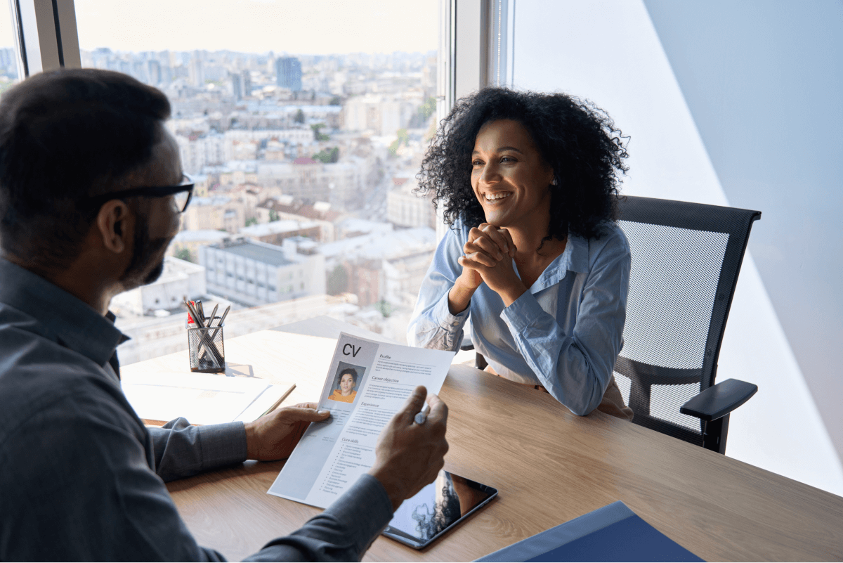 Friendly interview between hr director holding paper cv hiring for job female African American applicant manager sitting in contemporary office. Human resources recruitment