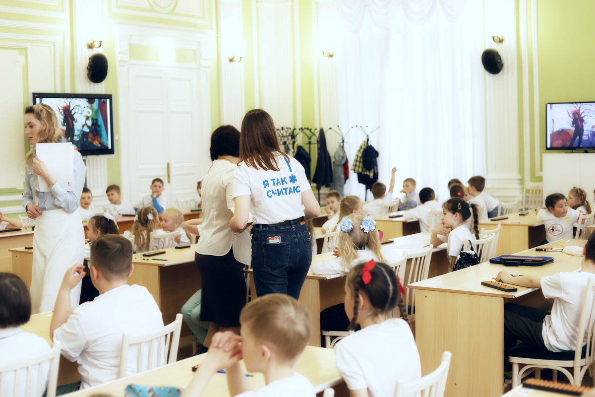 Региональная олимпиада ТГУ 2024 — дети за партами в зале, ассистент с табличкой Я ТАК СЧИТАЮ