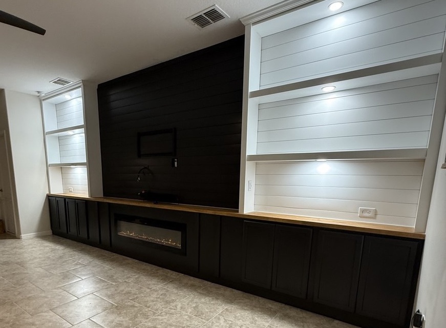 Wall-to-wall black shiplap entertainment center with lower cabinetry illuminated white shelving a wood countertop and linear fireplace in Atlanta