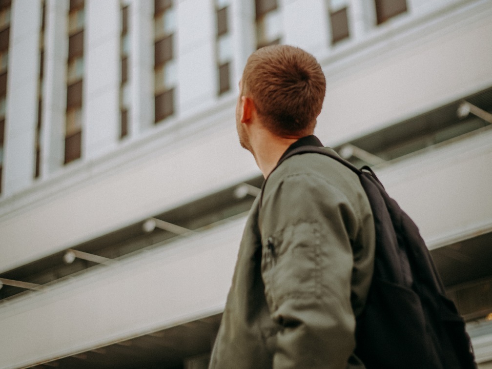 Ваня в зеленой куртке оборачивается на белое здание позади него