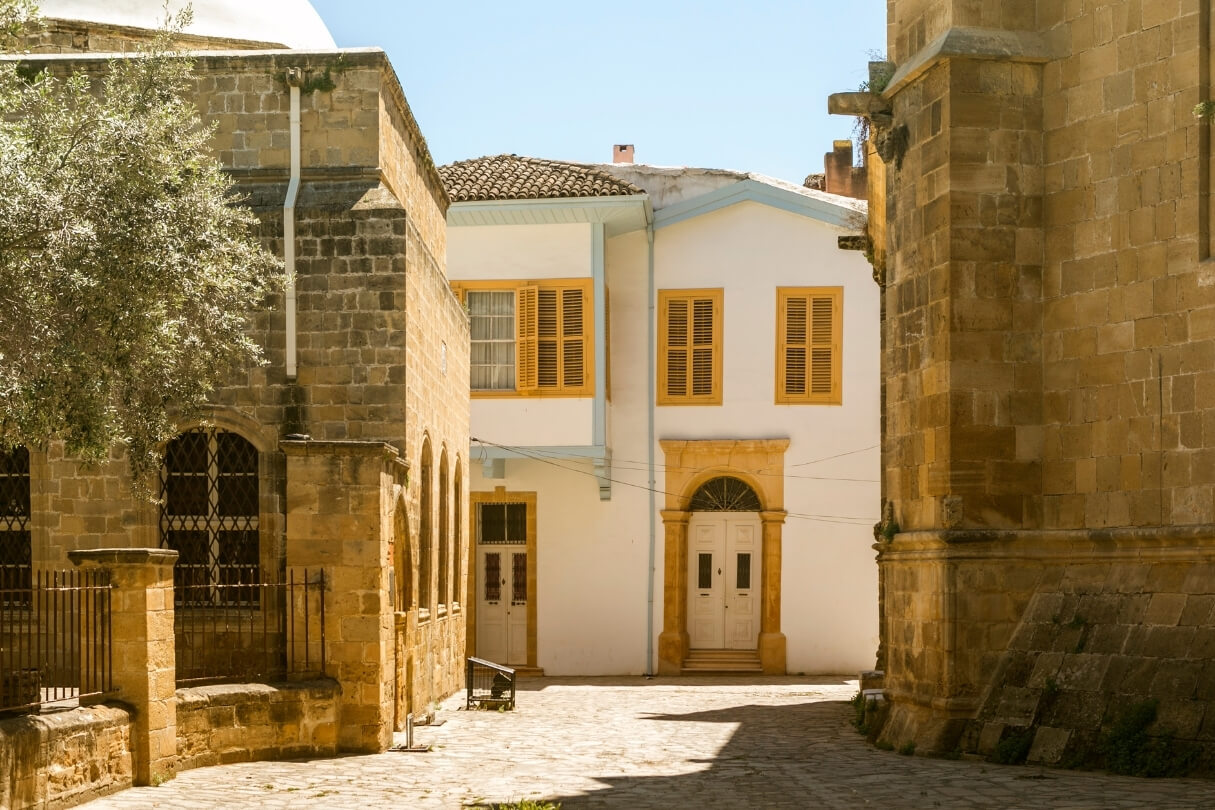 Тихий двор между каменными зданиями и домом с деревянными ставнями.