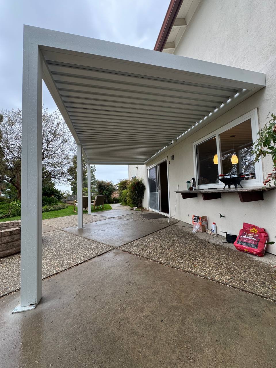 White motorized pergola with louvers in a more closed position over the concrete patio