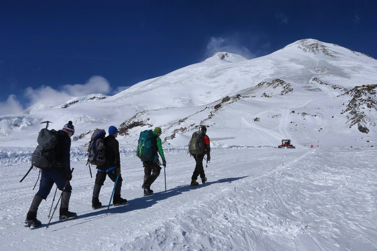 Four climbers walking in winter with the twin summits of Elbrus ahead