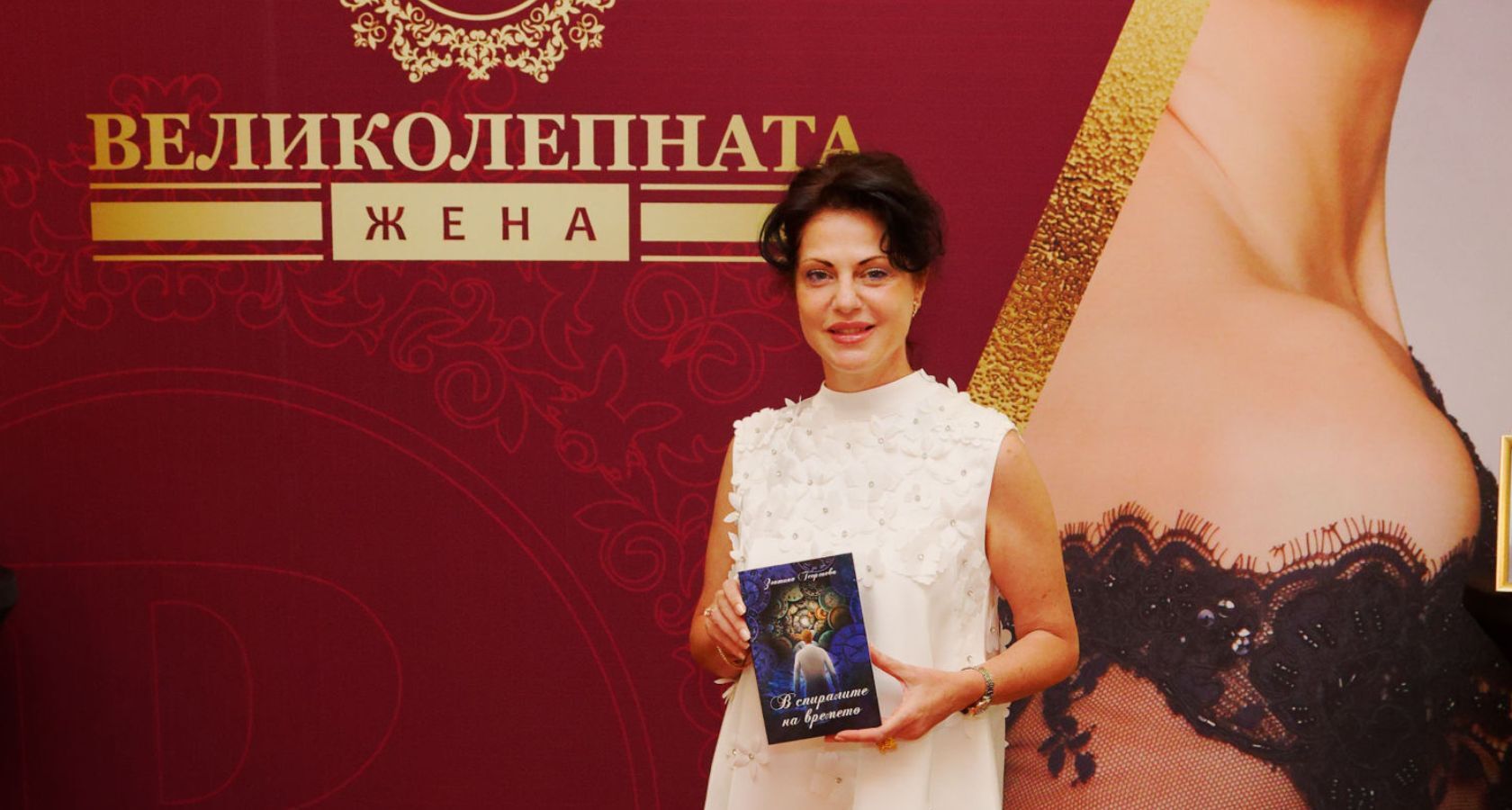 Златина Георгиева позира за снимка с книгата пред стената на Великолепната Жена на Официалната церемония Код ВЕЛИКОЛЕПНА