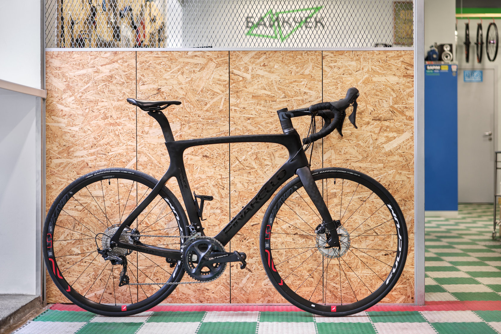Черный шоссейный велосипед Pinarello у стены из ОСБ в мастерской